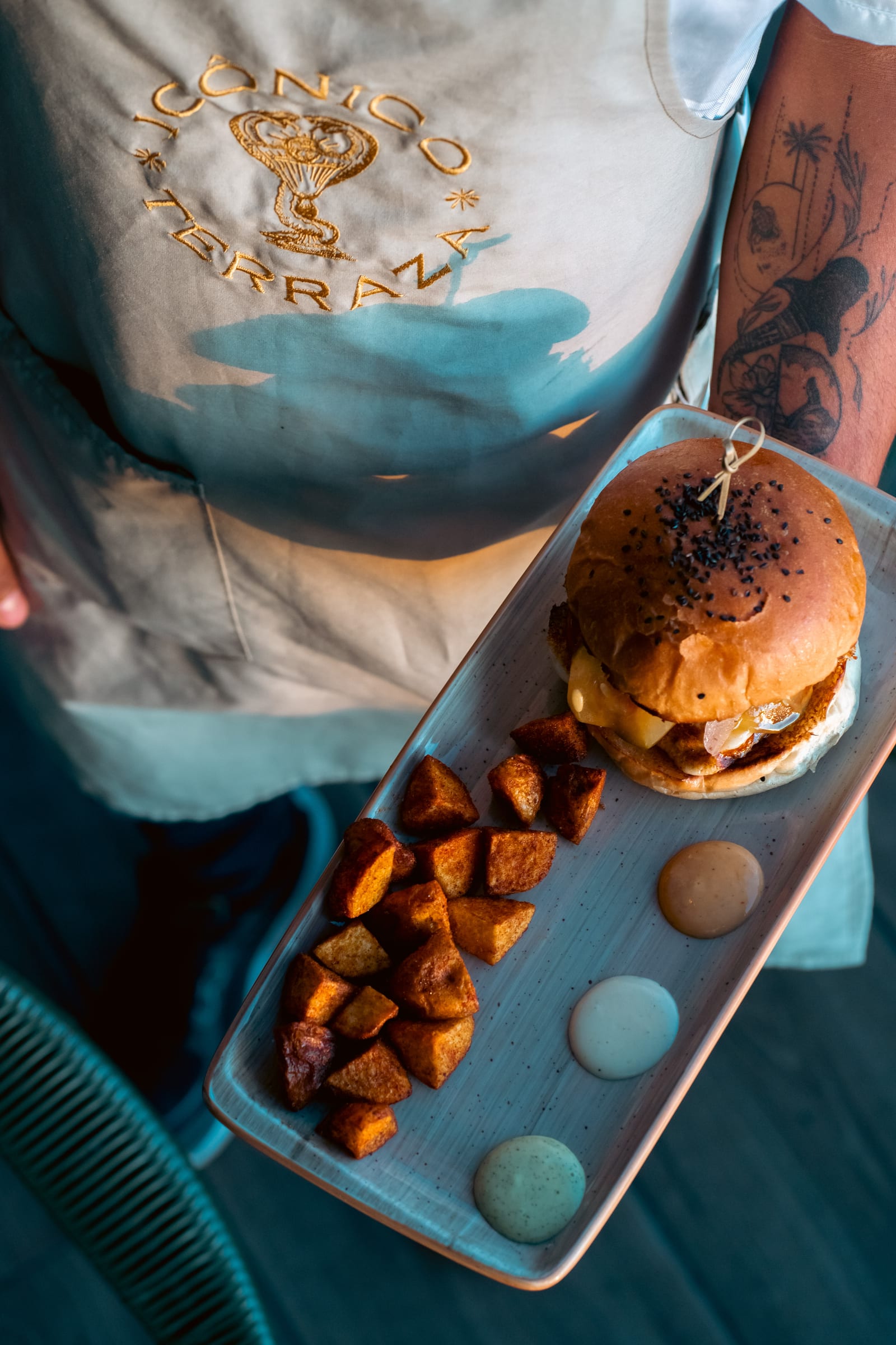 Hamburguesa de Icónico servida con papas criollas y salsas